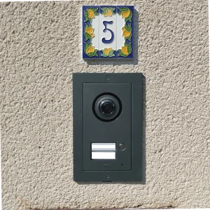 Un interphone vidéo noir avec caméra, monté sur un mur en stuc avec une plaque décorative numérotée "5".